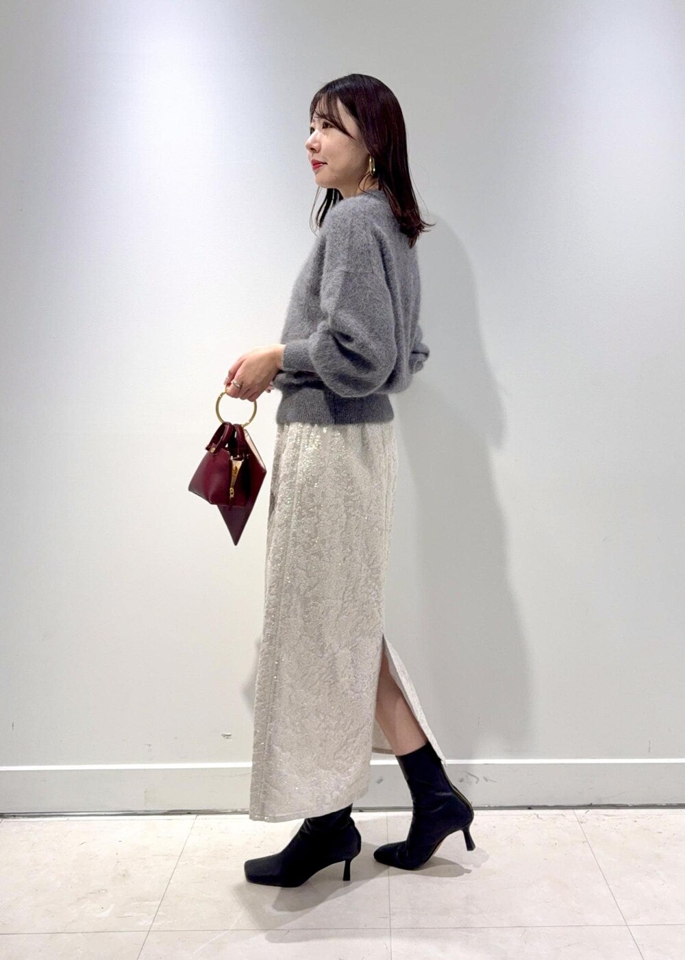 レッド系のショルダーバッグ、ブラック系のブーツ、グレー系のニット/セーターを着用したレディースの冬コーディネートの3枚目の写真