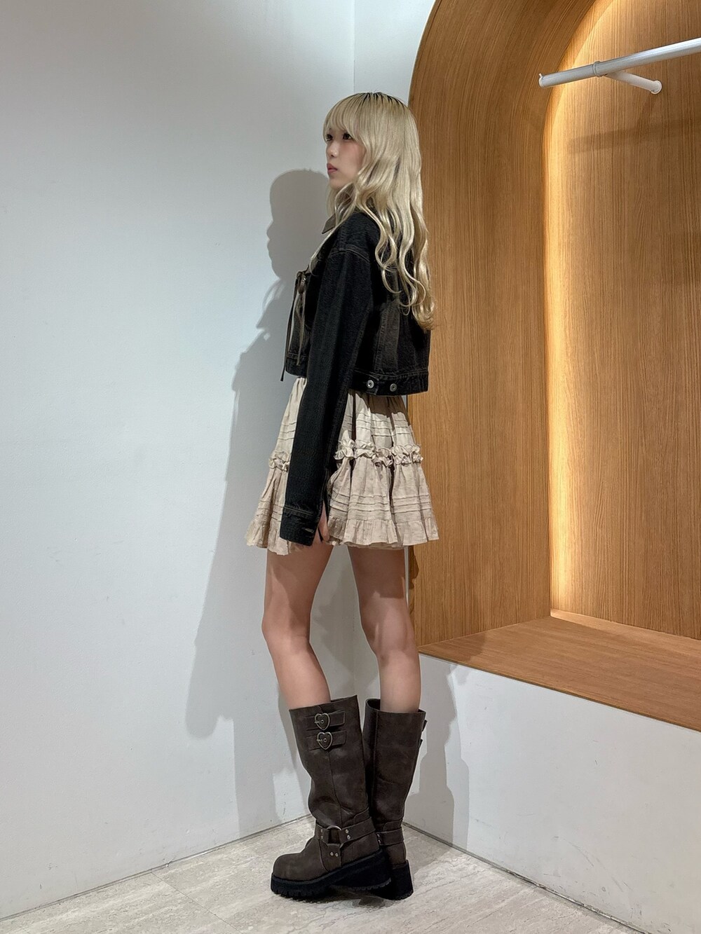 ベージュ系のスカート、ブラック系のデニムジャケット、ブラウン系のブーツを着用したレディースの夏コーディネートの2枚目の写真