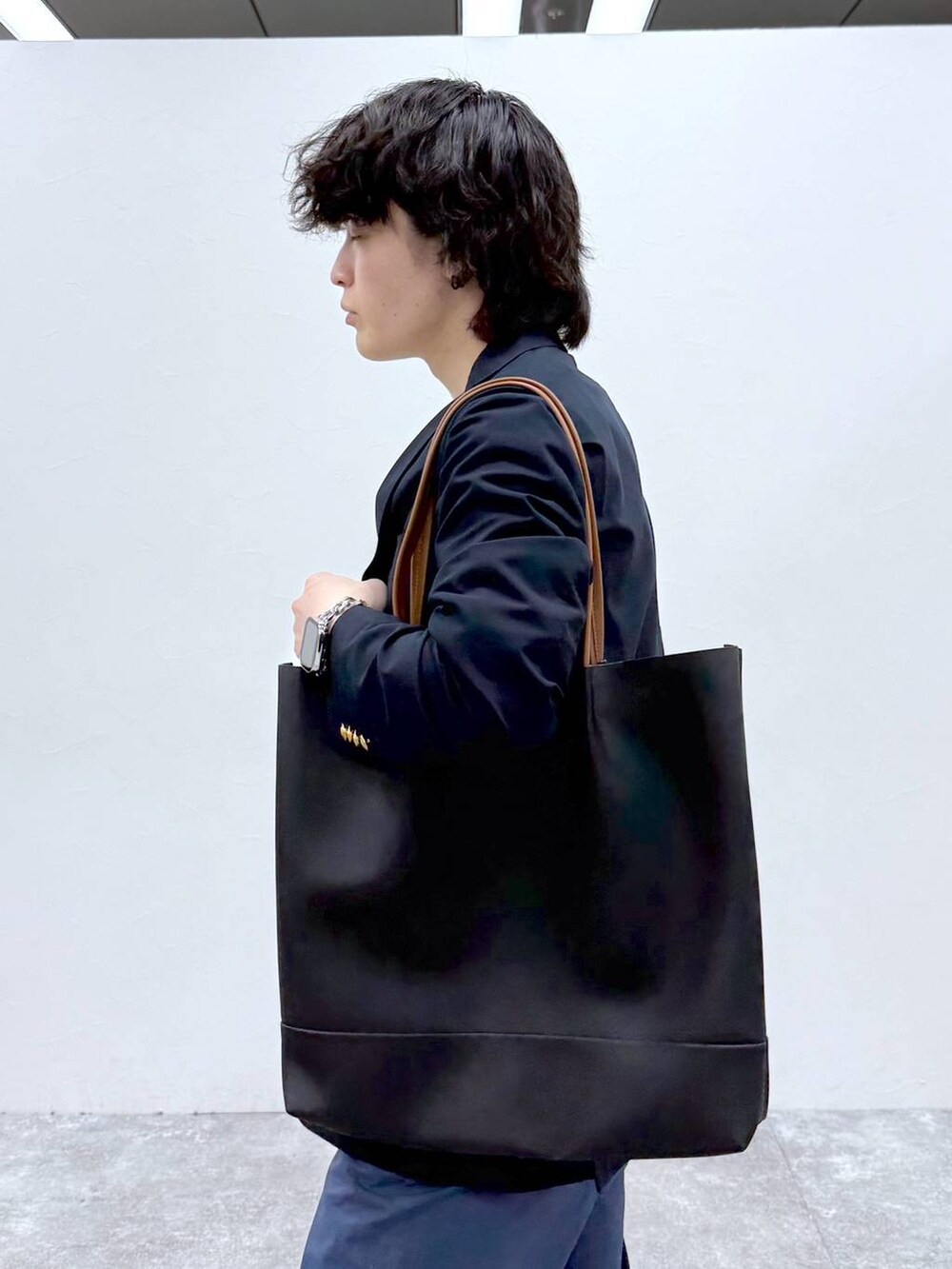ブラック系のトートバッグ、ブルー系のその他パンツ、ホワイト系のTシャツ/カットソーを着用したメンズの春コーディネートの6枚目の写真