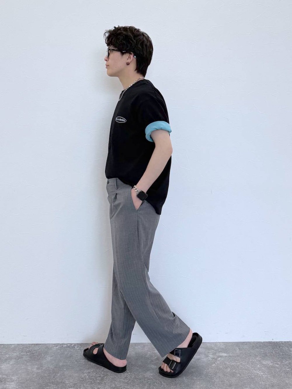 グレー系のスラックス、ブルー系のTシャツ/カットソー、ブラック系のサンダルを着用したメンズの夏コーディネートの4枚目の写真