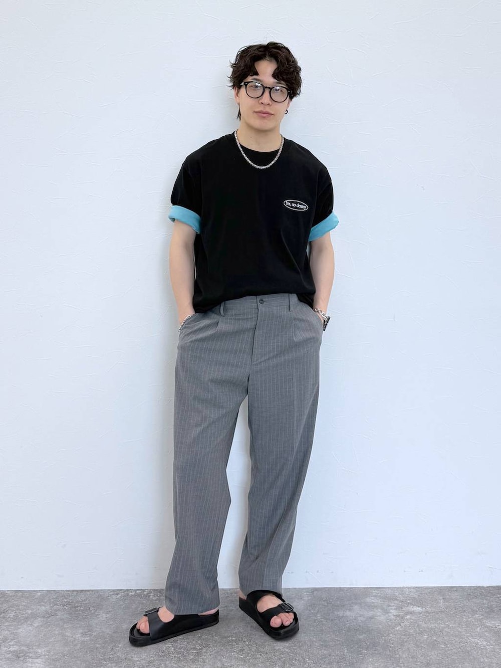グレー系のスラックス、ブルー系のTシャツ/カットソー、ブラック系のサンダルを着用したメンズの夏コーディネートの2枚目の写真