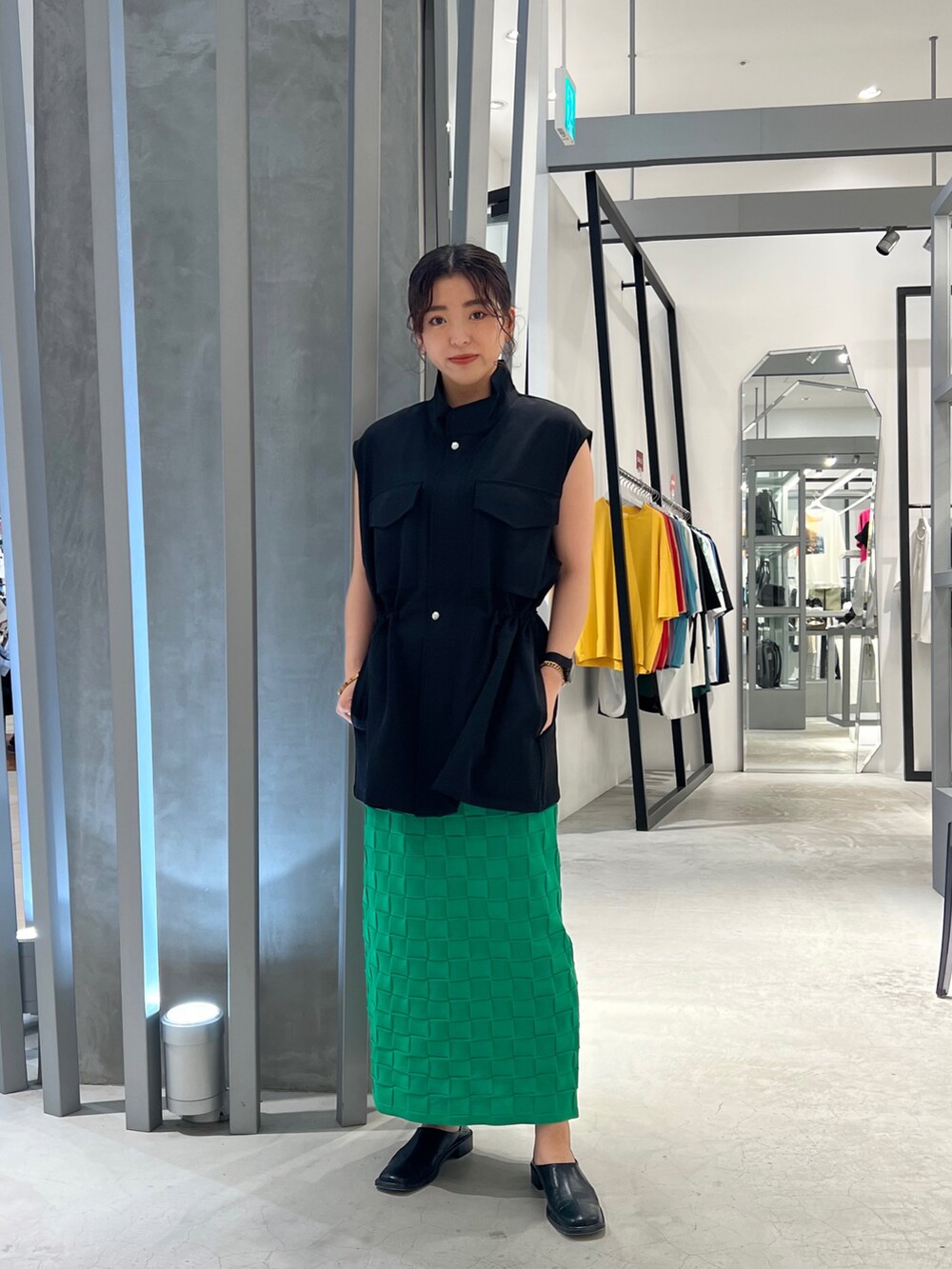 ブラック系のパンプス、グリーン系のスカート、ブラック系のベストを着用したレディースの夏コーディネートの2枚目の写真
