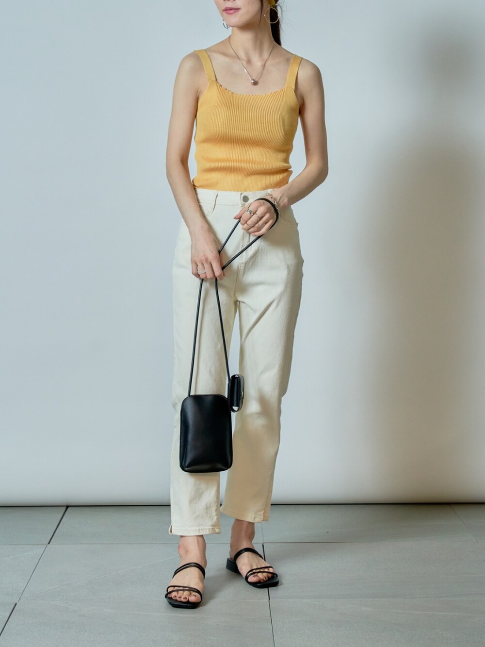 ホワイト系のデニムパンツ、イエロー系のタンクトップ、ブラック系のサンダルを着用したレディースの夏コーディネートの2枚目の写真