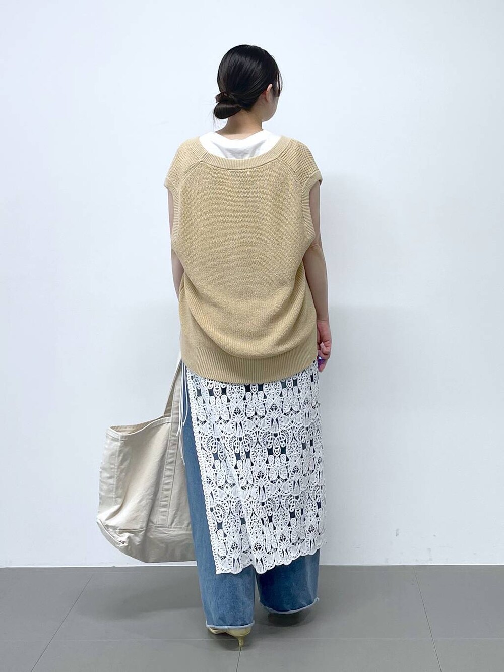 ブルー系のデニムパンツ、ホワイト系のタンクトップ、ベージュ系のベストを着用したレディースの春コーディネートの3枚目の写真