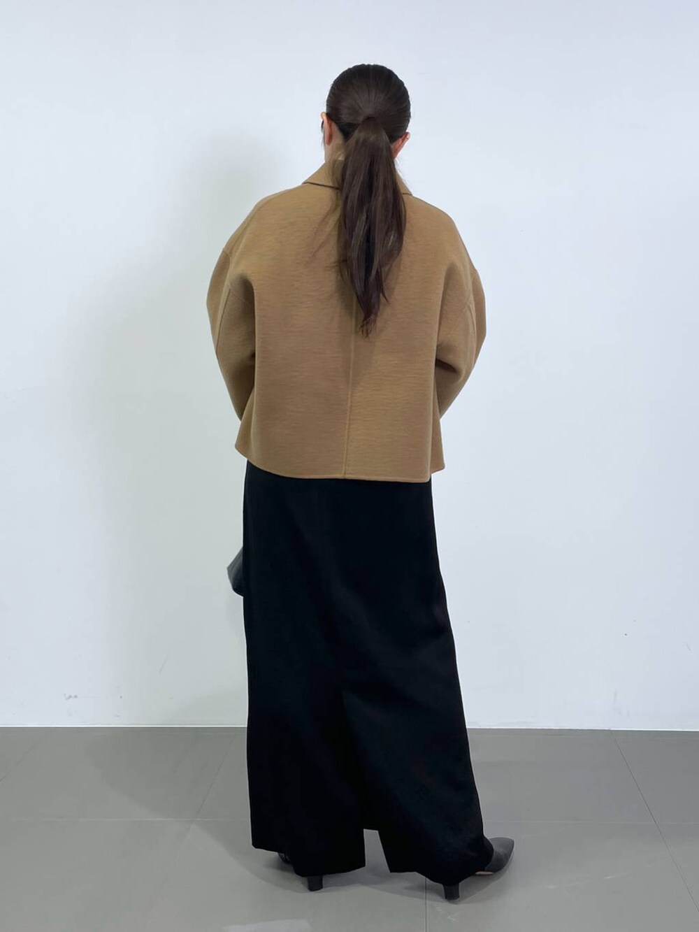 ブラック系のスカート、ベージュ系のその他アウター、ホワイト系のニット/セーターを着用したレディースの冬コーディネートの3枚目の写真