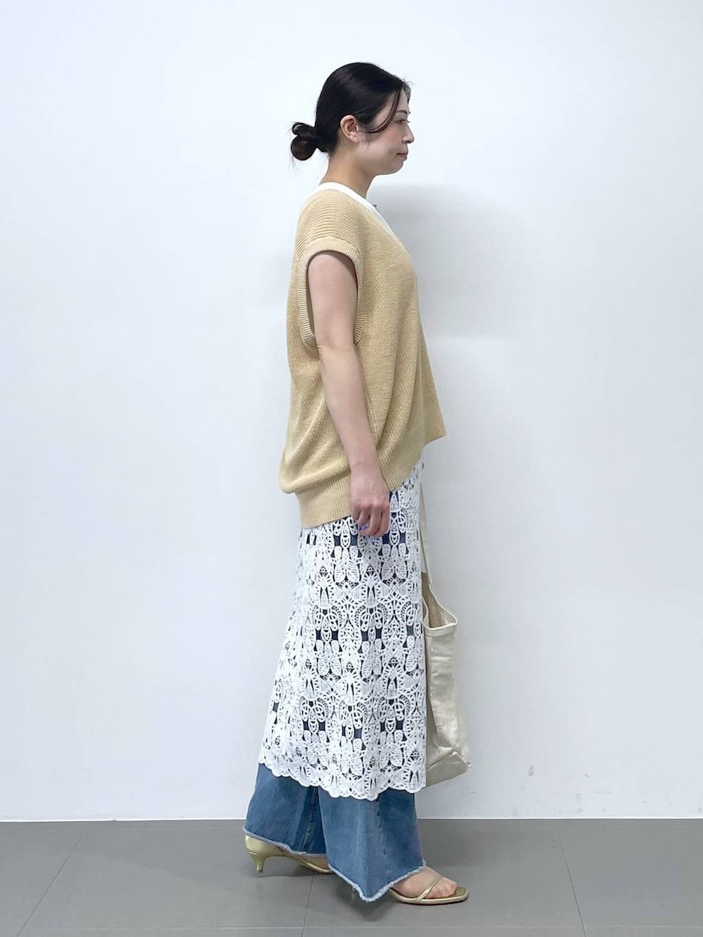 ブルー系のデニムパンツ、ホワイト系のタンクトップ、ベージュ系のベストを着用したレディースの春コーディネートの2枚目の写真