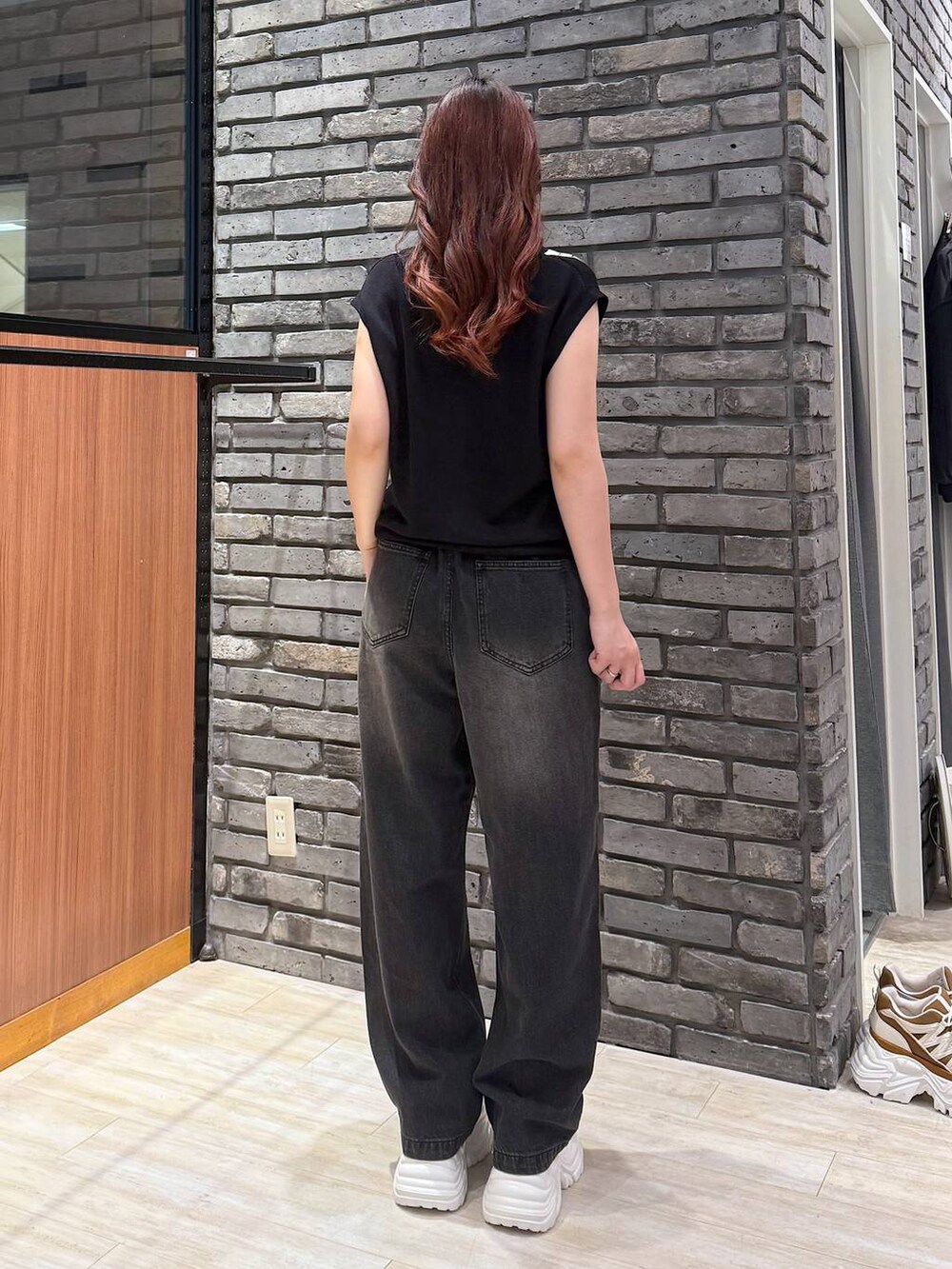 ホワイト系のスニーカー、ブラック系のデニムパンツ、ブラック系のベストを着用したレディースの秋コーディネートの3枚目の写真