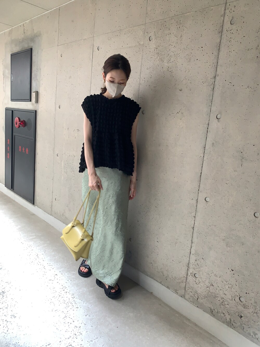 ブラック系のトップス、イエロー系のスカート、ブラック系のサンダルを着用したレディースの夏コーディネートの2枚目の写真