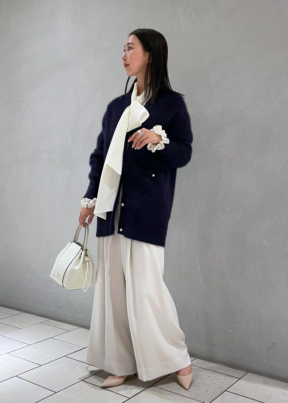 ホワイト系のハンドバッグ、ベージュ系のパンプス、ブルー系のカーディガン/ボレロを着用したレディースの冬コーディネートの2枚目の写真