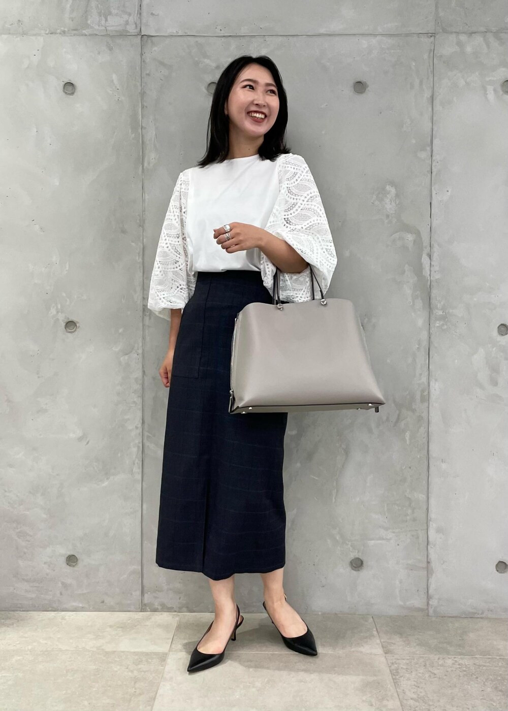 ブラック系のパンプス、グレー系のトートバッグ、ブルー系のスカートを着用したレディースの秋コーディネートの2枚目の写真