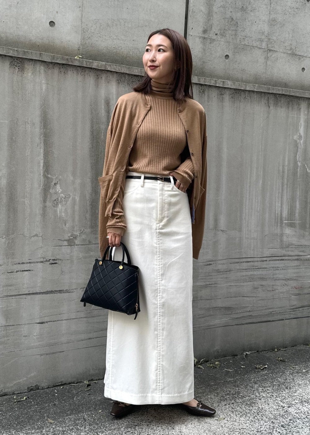 ブラウン系のパンプス、ブラック系のハンドバッグ、ホワイト系のスカートを着用したレディースの冬コーディネートの4枚目の写真