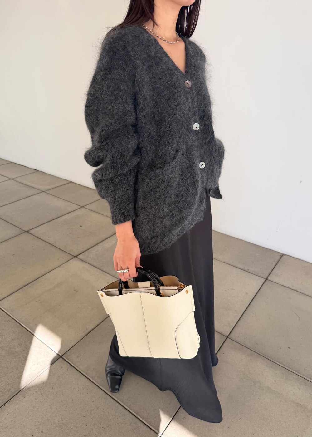 ホワイト系のハンドバッグ、ブラック系のスカート、ブラック系のブーツを着用したレディースの秋コーディネートの5枚目の写真