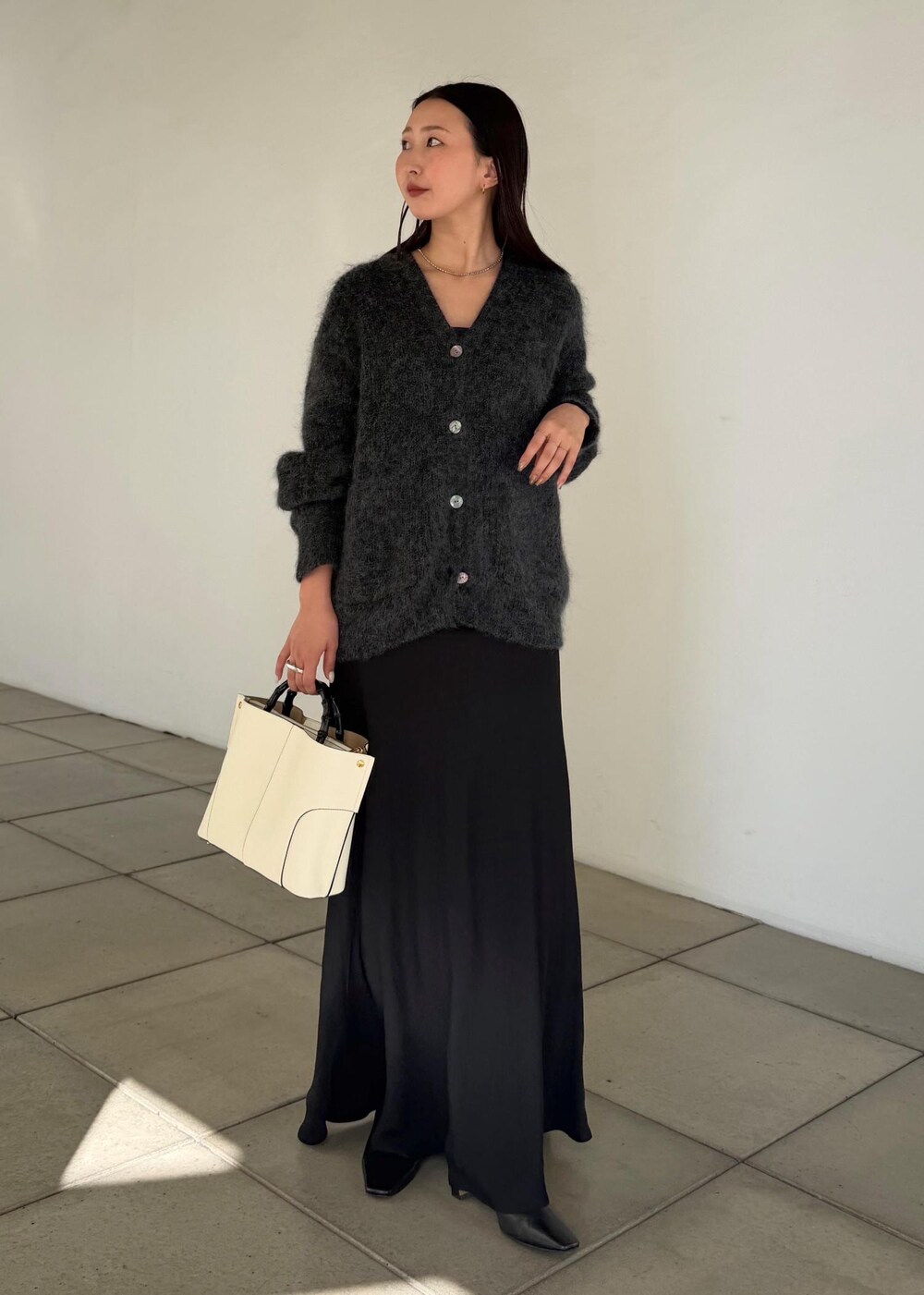 ホワイト系のハンドバッグ、ブラック系のスカート、ブラック系のブーツを着用したレディースの秋コーディネートの4枚目の写真