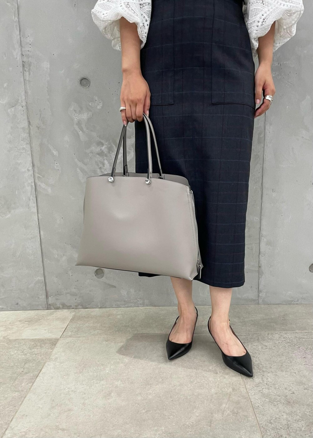 ブラック系のパンプス、グレー系のトートバッグ、ブルー系のスカートを着用したレディースの秋コーディネートの8枚目の写真