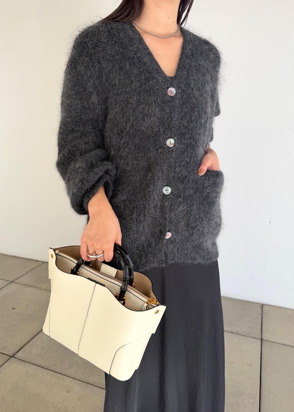 ホワイト系のハンドバッグ、ブラック系のスカート、ブラック系のブーツを着用したレディースの秋コーディネートの8枚目の写真