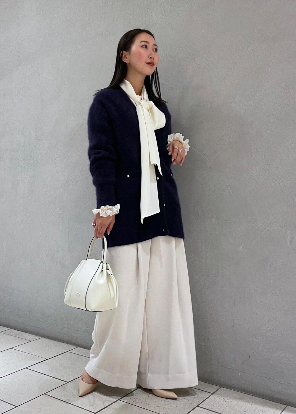 ホワイト系のハンドバッグ、ベージュ系のパンプス、ブルー系のカーディガン/ボレロを着用したレディースの冬コーディネートの3枚目の写真