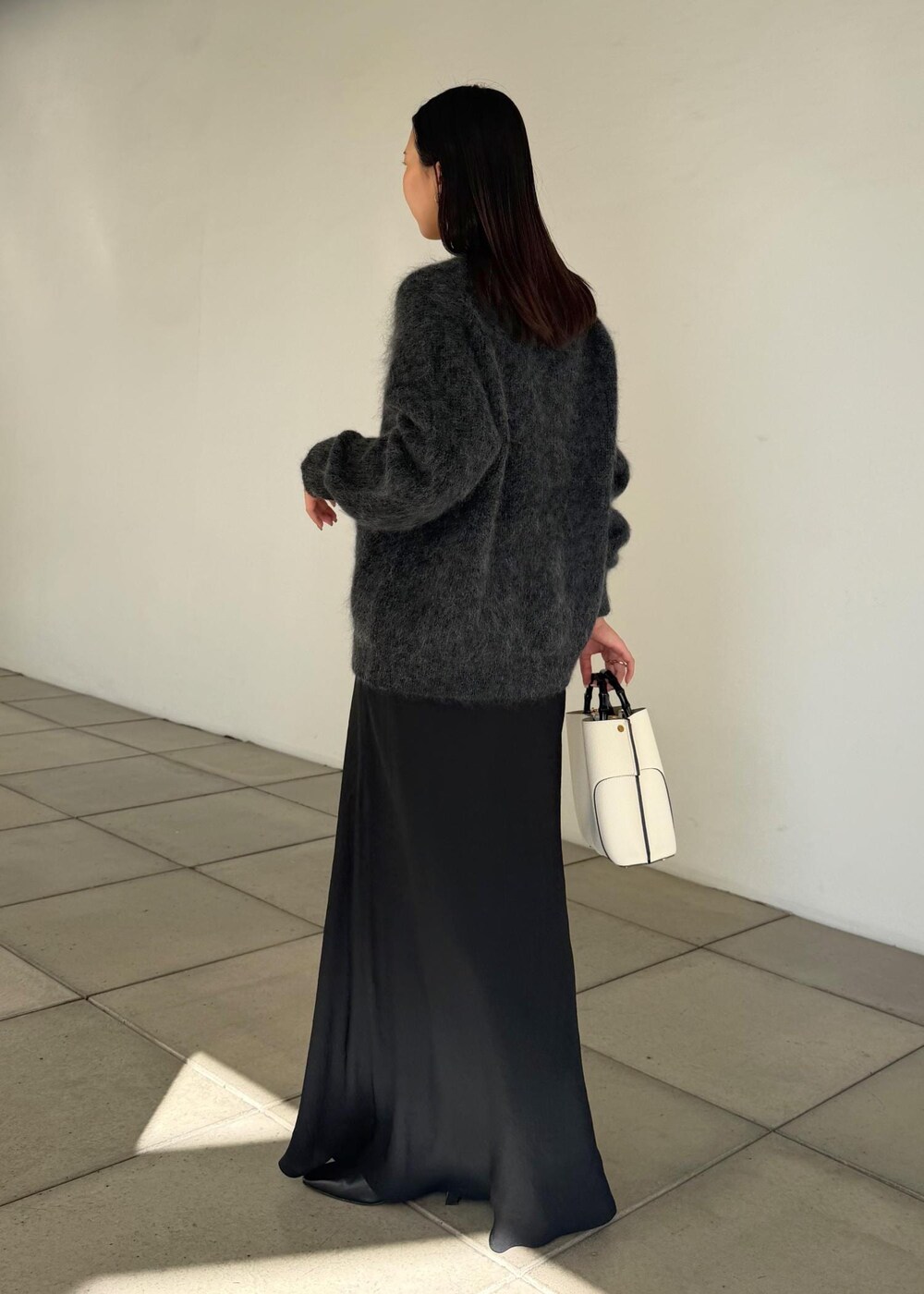 ホワイト系のハンドバッグ、ブラック系のスカート、ブラック系のブーツを着用したレディースの秋コーディネートの2枚目の写真