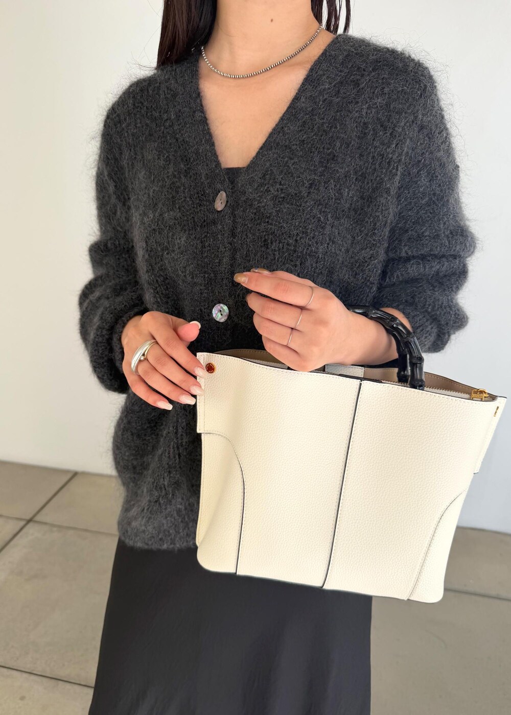 ホワイト系のハンドバッグ、ブラック系のスカート、ブラック系のブーツを着用したレディースの秋コーディネートの7枚目の写真