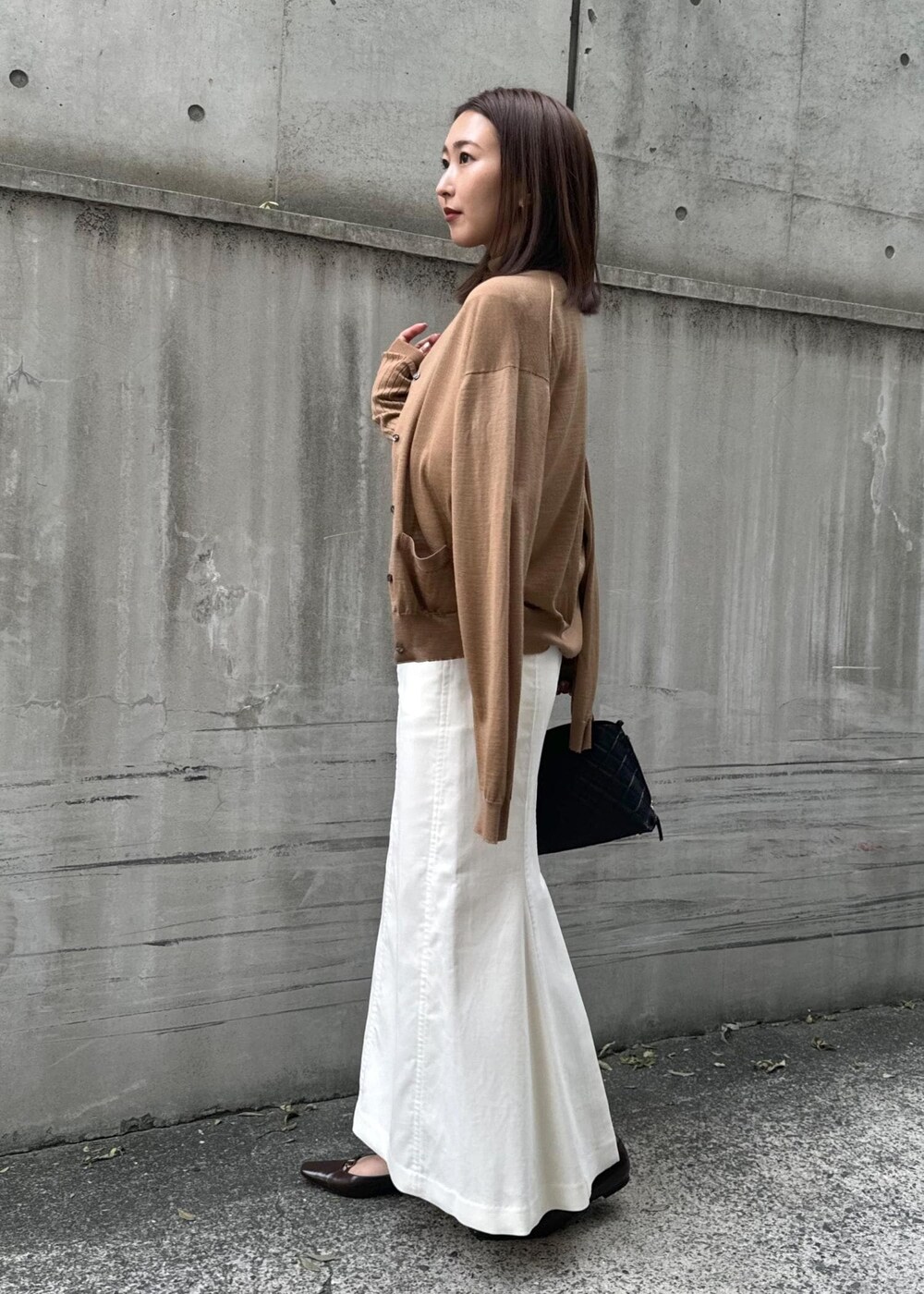 ブラウン系のパンプス、ブラック系のハンドバッグ、ホワイト系のスカートを着用したレディースの冬コーディネートの2枚目の写真