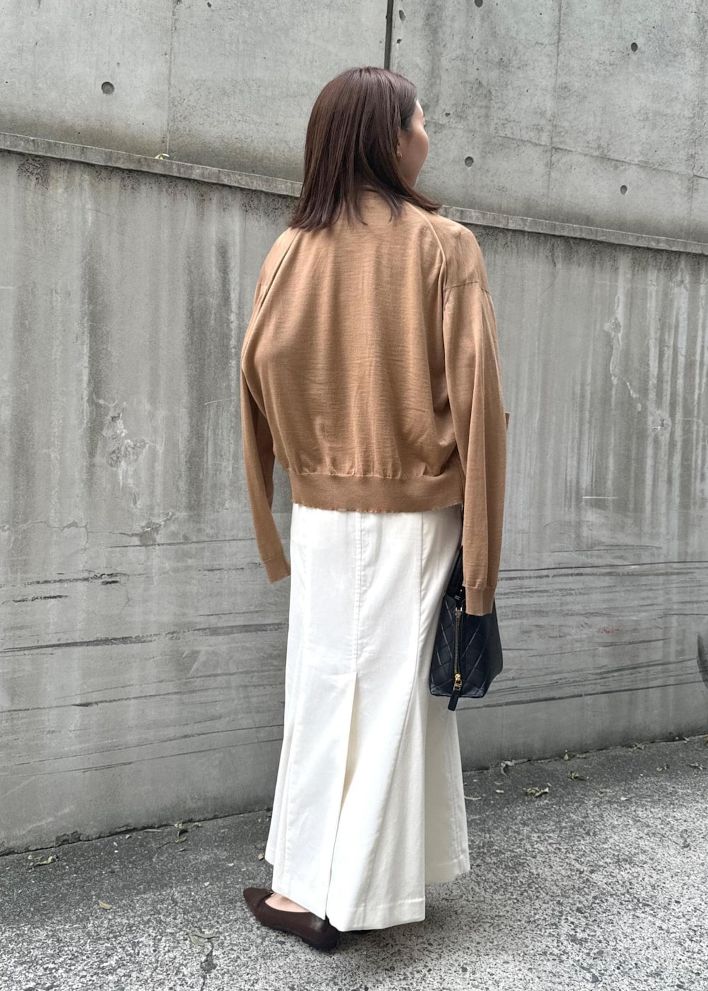 ブラウン系のパンプス、ブラック系のハンドバッグ、ホワイト系のスカートを着用したレディースの冬コーディネートの3枚目の写真