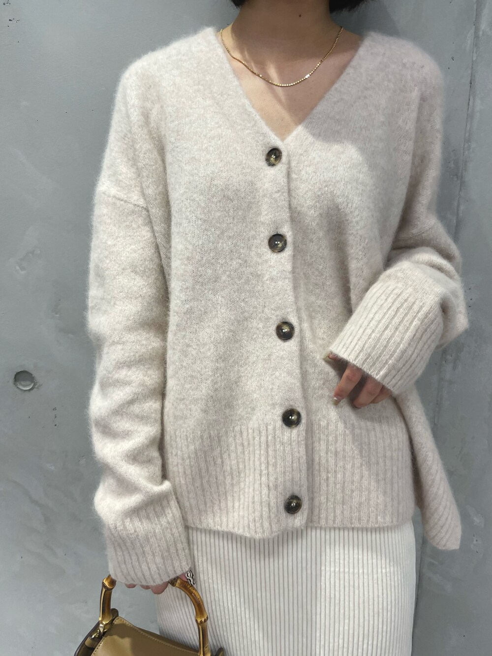 ベージュ系のカーディガン/ボレロ、ホワイト系のスカート、イエロー系のハンドバッグを着用したレディースの秋コーディネートの2枚目の写真