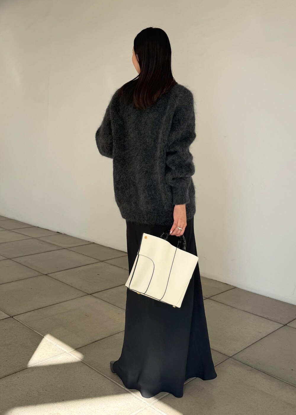 ホワイト系のハンドバッグ、ブラック系のスカート、ブラック系のブーツを着用したレディースの秋コーディネートの3枚目の写真
