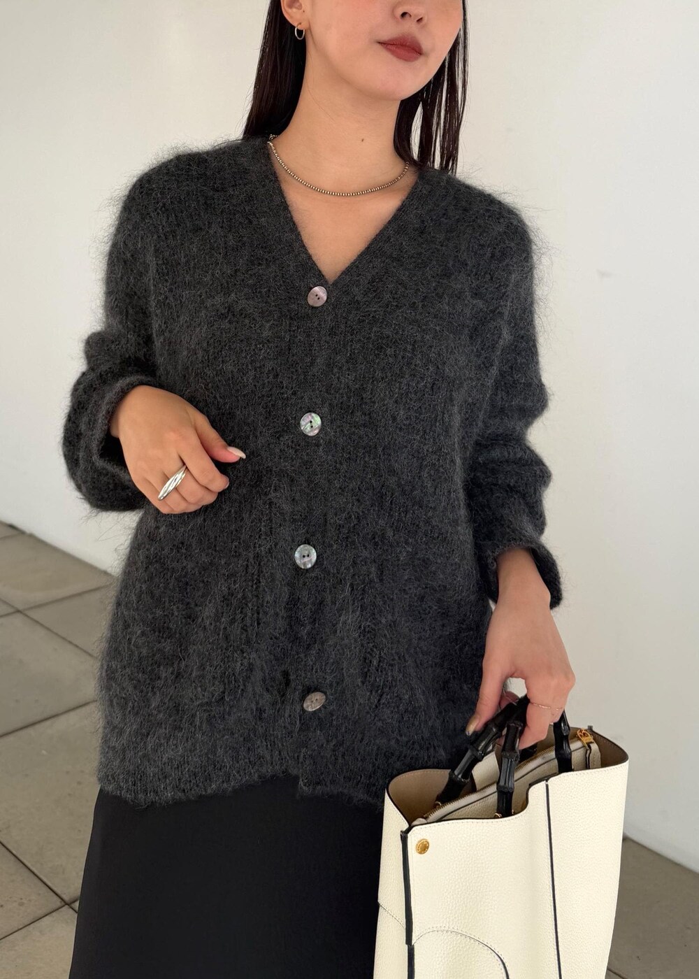 ホワイト系のハンドバッグ、ブラック系のスカート、ブラック系のブーツを着用したレディースの秋コーディネートの6枚目の写真