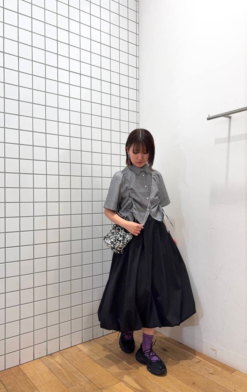 シルバー系のショルダーバッグ、ブラック系のスニーカー、ブラック系のスカートを着用したレディースの春コーディネートの2枚目の写真