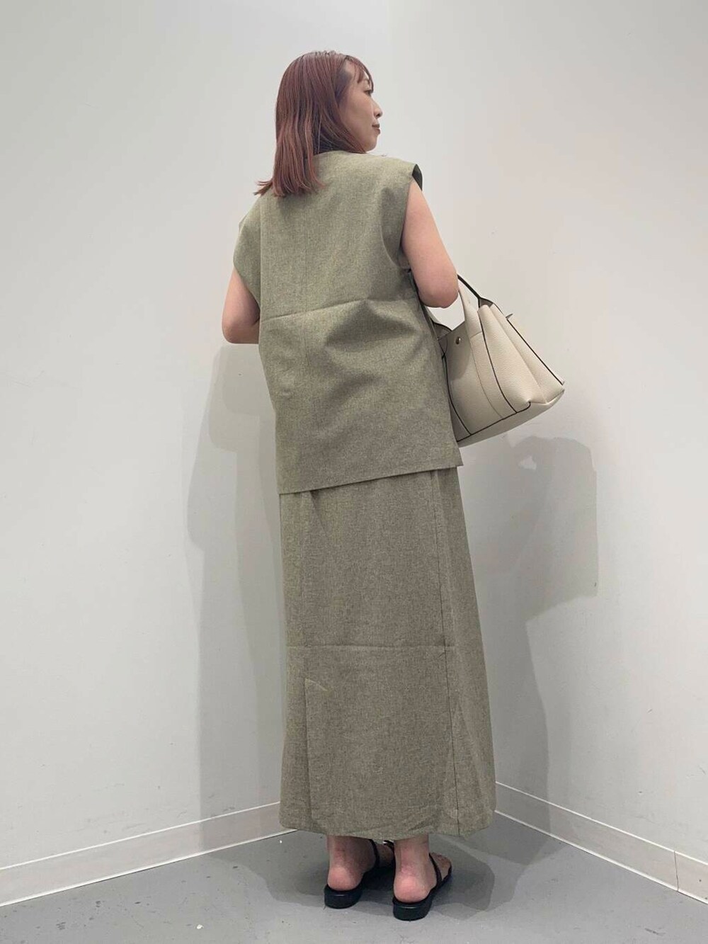 ホワイト系のトートバッグ、ブラック系のサンダル、グリーン系のベストを着用したレディースの夏コーディネートの3枚目の写真