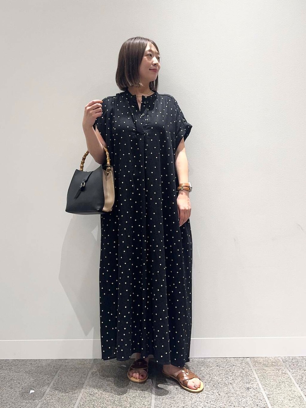 ブラウン系のサンダル、ブラック系のハンドバッグ、ブラック系のワンピースを着用したレディースの夏コーディネートの2枚目の写真