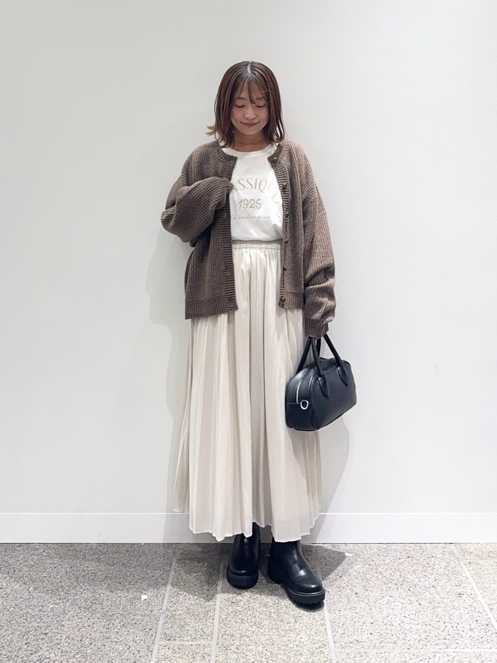 ブラウン系のカーディガン/ボレロ、ホワイト系のスカート、ブラック系のショルダーバッグを着用したレディースの秋コーディネートの4枚目の写真