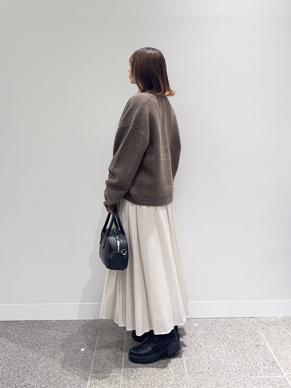 ブラウン系のカーディガン/ボレロ、ホワイト系のスカート、ブラック系のショルダーバッグを着用したレディースの秋コーディネートの2枚目の写真