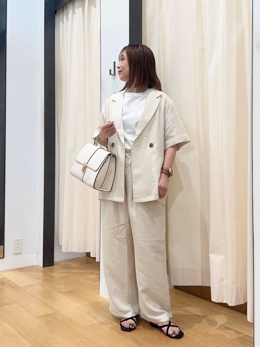 ホワイト系のハンドバッグ、ブラック系のサンダル、ホワイト系のTシャツ/カットソーを着用したレディースの夏コーディネートの2枚目の写真