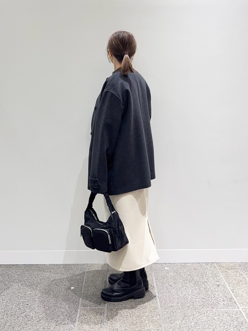 グレー系のピーコート、ブラウン系のニット/セーター、ホワイト系のスカートを着用したレディースの冬コーディネートの3枚目の写真