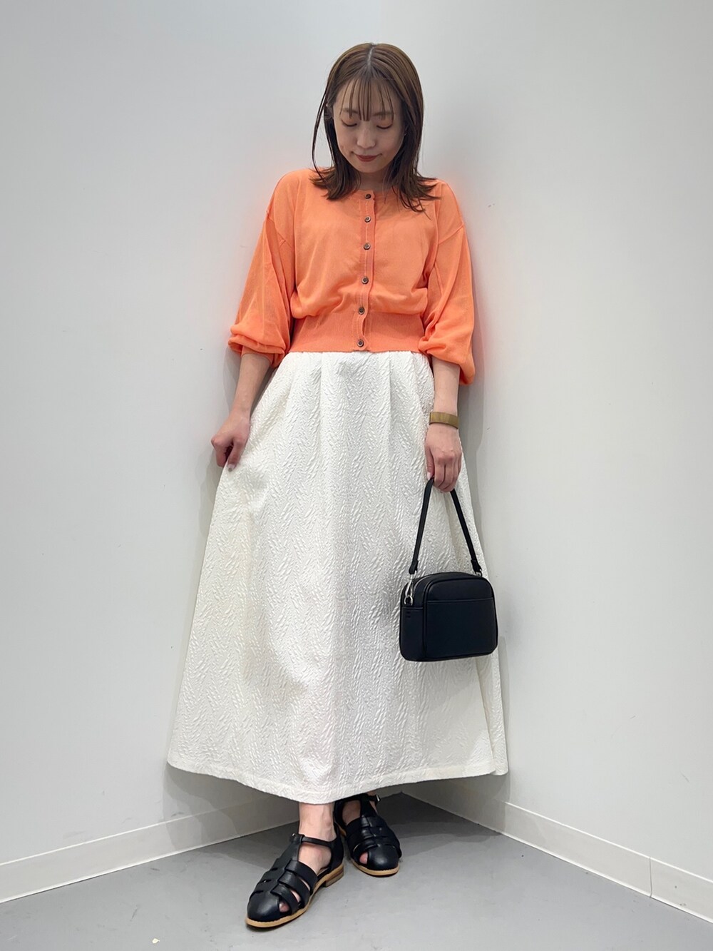 オレンジ系のカーディガン/ボレロ、ホワイト系のスカート、ブラック系のショルダーバッグを着用したレディースの春コーディネートの4枚目の写真
