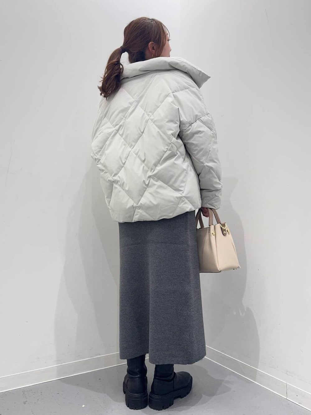 ホワイト系のトートバッグ、ブラック系のブーツ、グレー系のダウンジャケット/コートを着用したレディースの冬コーディネートの3枚目の写真