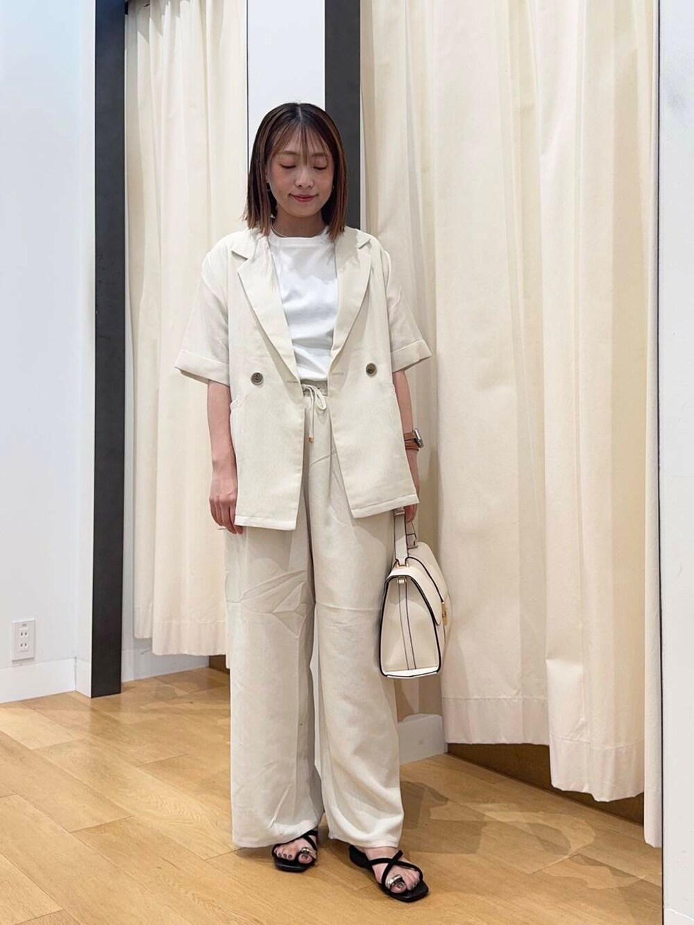 ホワイト系のハンドバッグ、ブラック系のサンダル、ホワイト系のTシャツ/カットソーを着用したレディースの夏コーディネートの5枚目の写真