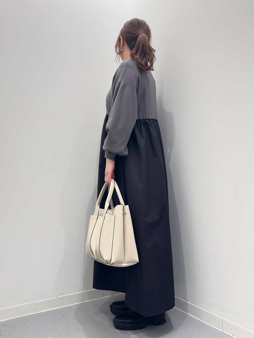 ブラック系のブーツ、ホワイト系のトートバッグ、グレー系のワンピースを着用したレディースの冬コーディネートの2枚目の写真