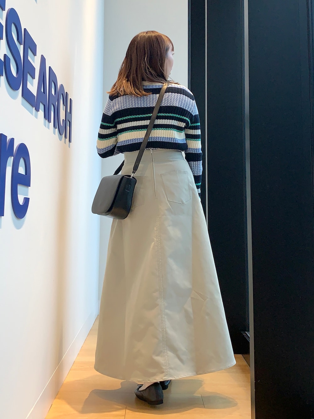 ベージュ系のカバーオール、ブルー系のニット/セーター、グリーン系のスカートを着用したレディースの春コーディネートの5枚目の写真