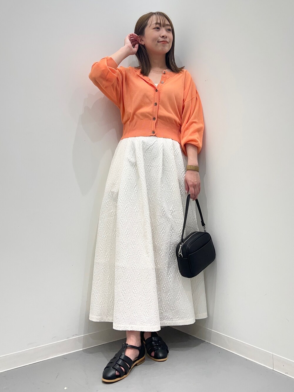 オレンジ系のカーディガン/ボレロ、ホワイト系のスカート、ブラック系のショルダーバッグを着用したレディースの春コーディネートの3枚目の写真