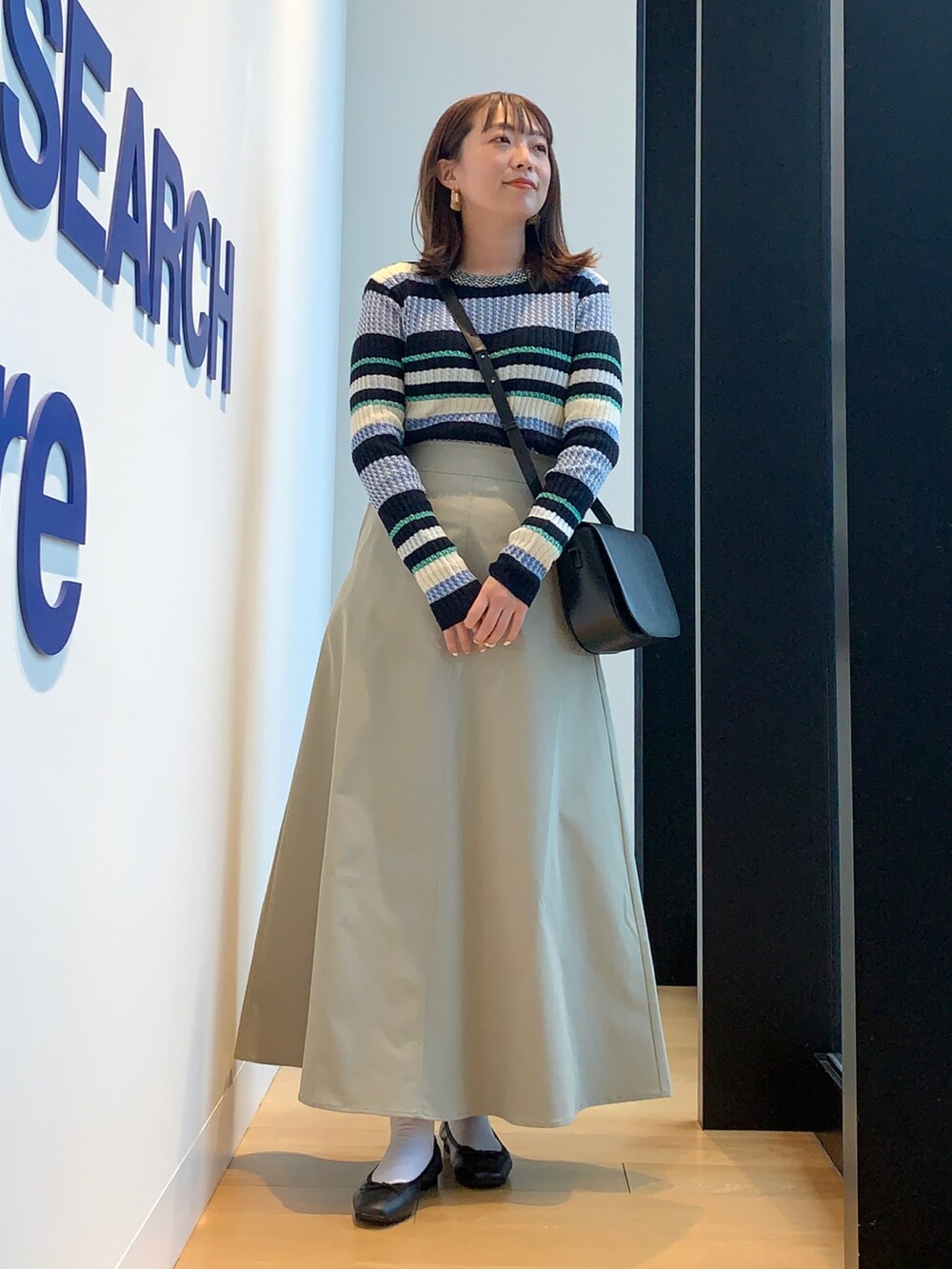 ベージュ系のカバーオール、ブルー系のニット/セーター、グリーン系のスカートを着用したレディースの春コーディネートの4枚目の写真