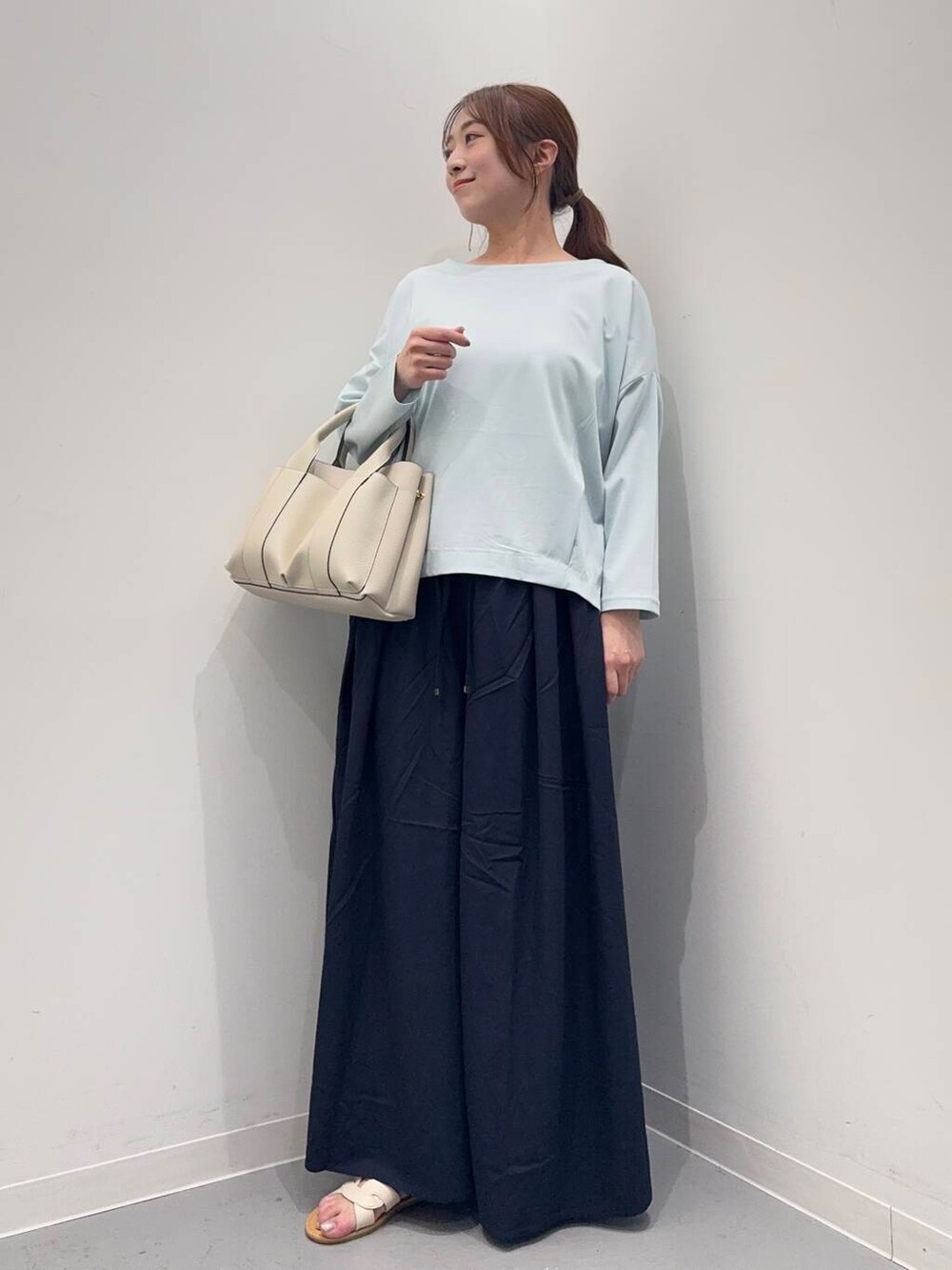 ホワイト系のトートバッグ、ブルー系のTシャツ/カットソー、ホワイト系のサンダルを着用したレディースの春コーディネートの2枚目の写真