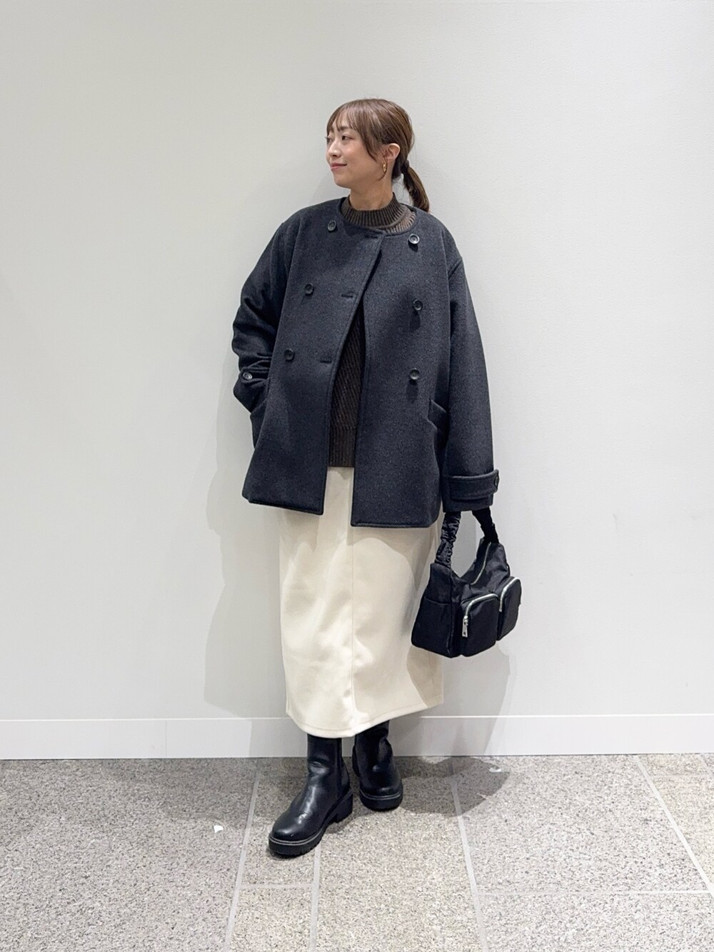 グレー系のピーコート、ブラウン系のニット/セーター、ホワイト系のスカートを着用したレディースの冬コーディネートの2枚目の写真