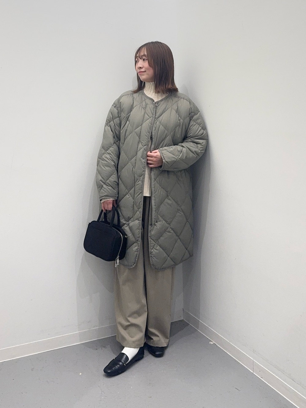 グリーン系のダウンジャケット/コート、ホワイト系のニット/セーター、ブラック系のボストンバッグを着用したレディースの冬コーディネートの3枚目の写真