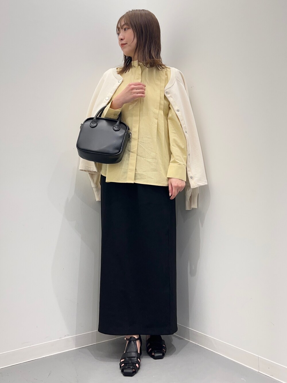 イエロー系のシャツ/ブラウス、ブラック系のスカート、ホワイト系のカーディガン/ボレロを着用したレディースの春コーディネートの2枚目の写真