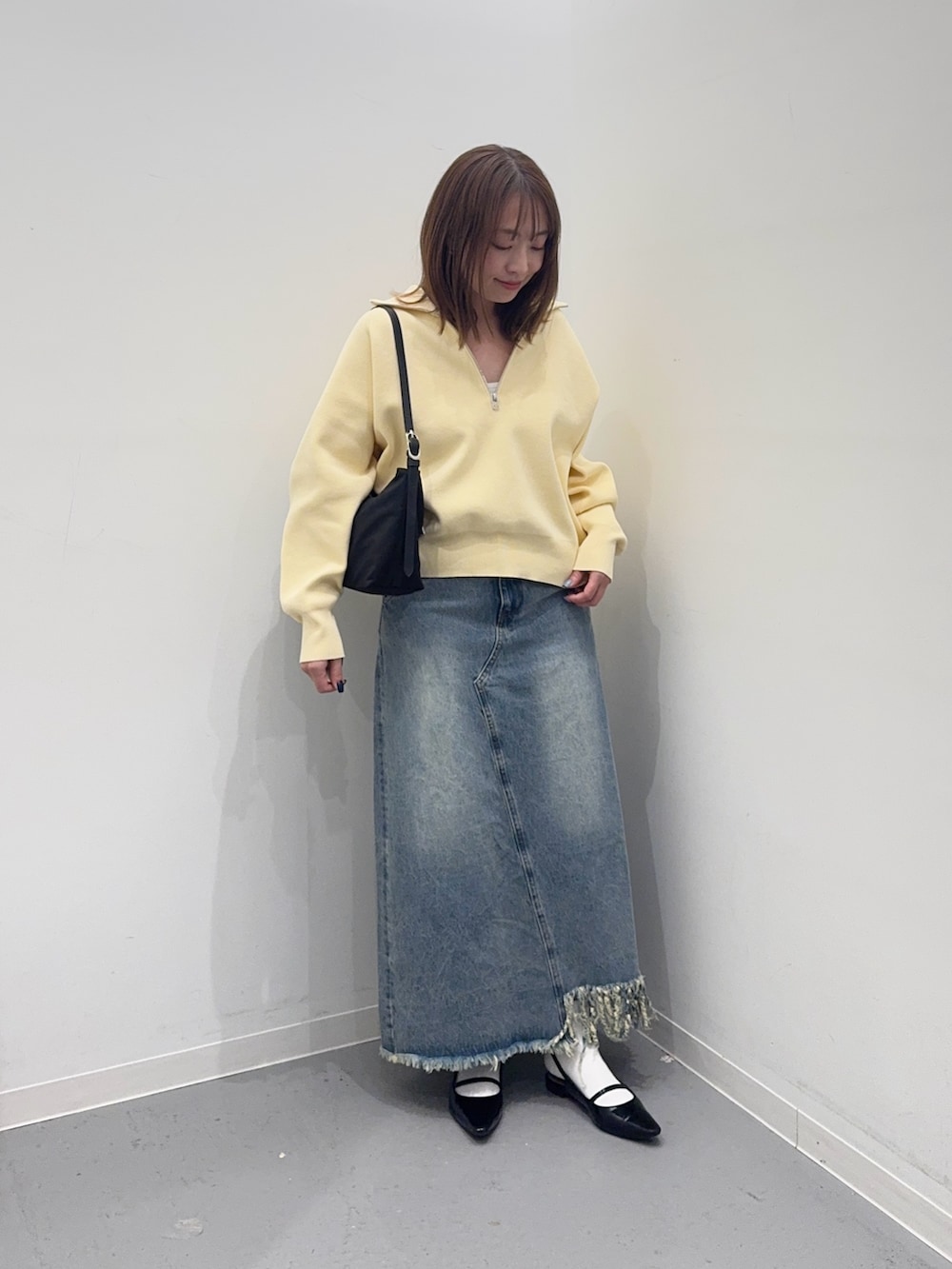 イエロー系のスウェット、ブルー系のスカート、ブラック系のショルダーバッグを着用したレディースの冬コーディネートの2枚目の写真