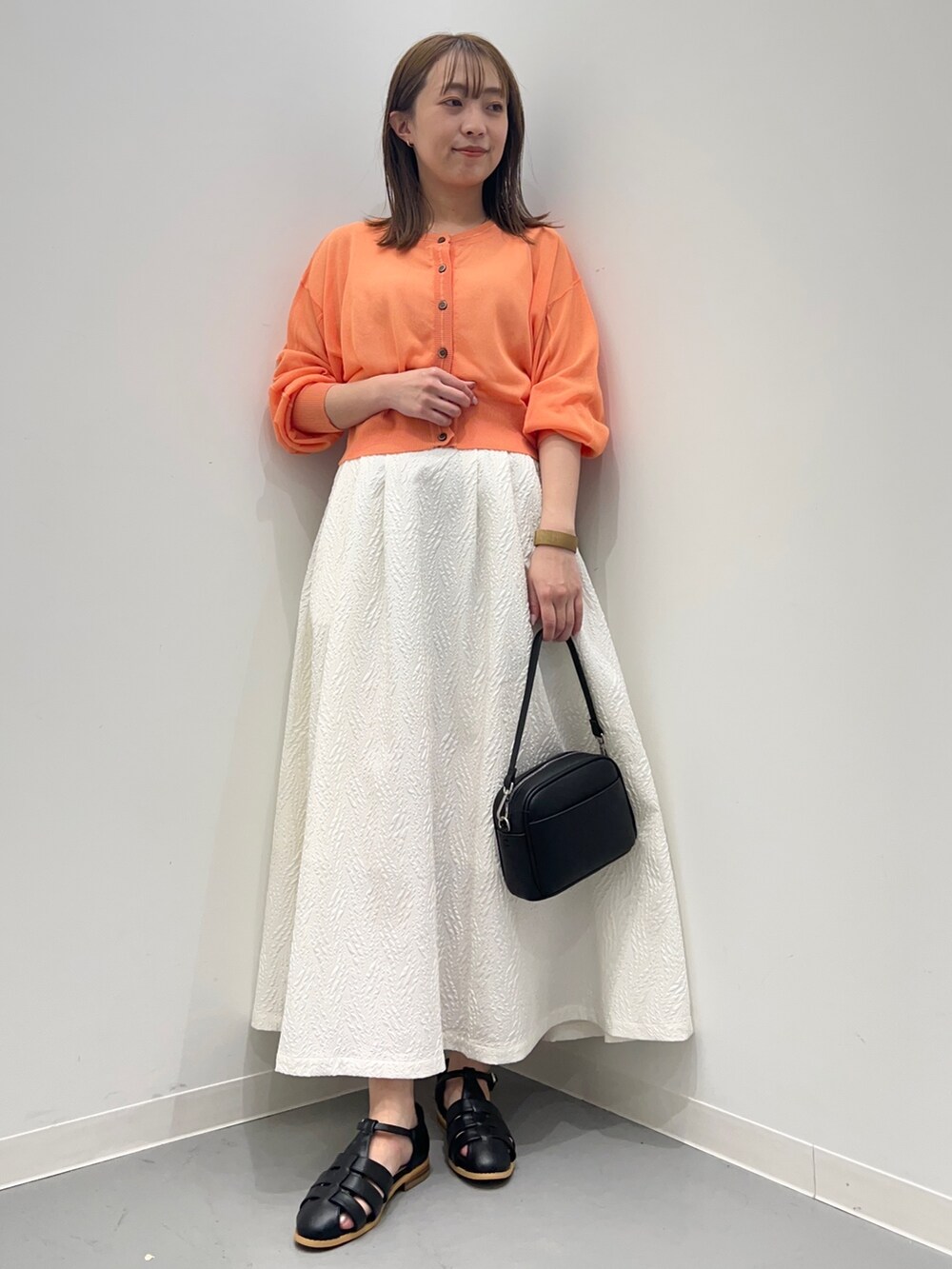 オレンジ系のカーディガン/ボレロ、ホワイト系のスカート、ブラック系のショルダーバッグを着用したレディースの春コーディネートの2枚目の写真