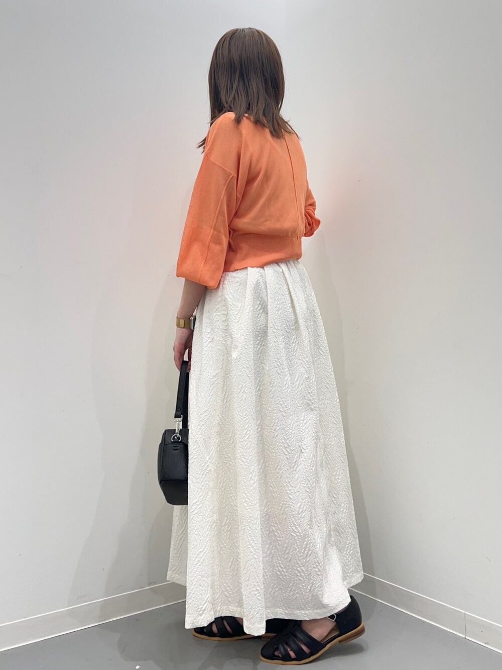 オレンジ系のカーディガン/ボレロ、ホワイト系のスカート、ブラック系のショルダーバッグを着用したレディースの春コーディネートの5枚目の写真