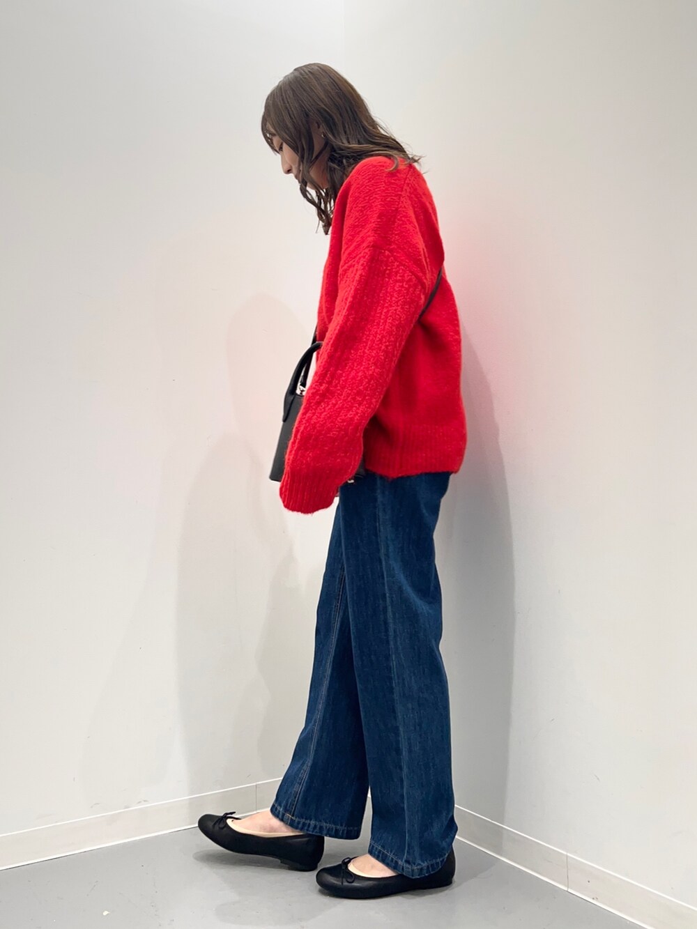 レッド系のニット/セーター、ブルー系のデニムパンツを着用したレディースの秋コーディネートの3枚目の写真