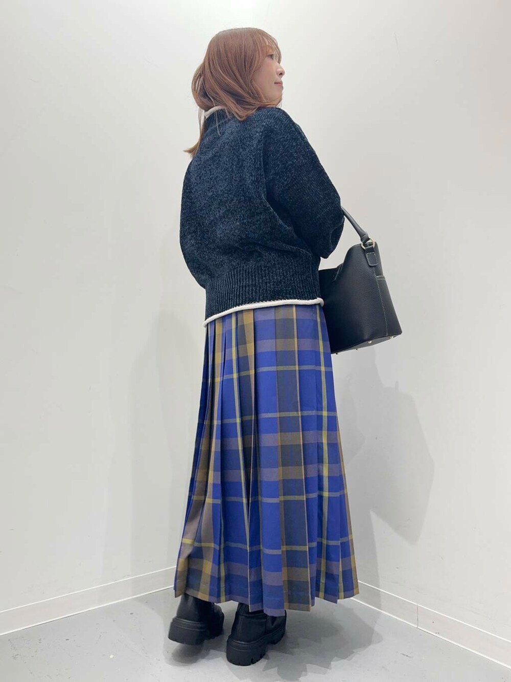 ブラック系のハンドバッグ、ブラック系のブーツ、ブルー系のスカートを着用したレディースの秋コーディネートの3枚目の写真